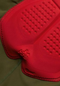 Rode gevoerde ruimte met een textuur oppervlak, gestikt aan groene stof. Heeft verhoogde stippen voor grip en een zichtbaar merkimpressie op de padding.
