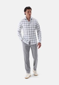 Camicia a maniche lunghe a righe bianche e grigie, abbinata a pantaloni grigi chiari e sneakers color crema. Tessuto morbido, vestibilità sartoriale.