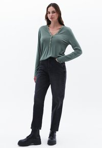 Camisa de botones de manga larga en un verde claro, combinada con vaqueros negros de cintura alta y botas negras con cordones, con un corte relajado y textura suave.