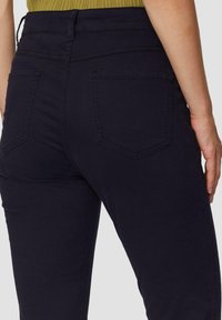 Donker marineblauwe skinny jeans met een gladde textuur, voorzien van een middenhoogte taille, achterzakken met een lichte punt en subtiele stiksel details.