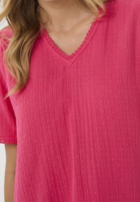 Rosa kurzärmliges Oberteil mit V-Ausschnitt, strukturiertem Stoff mit erhabenen Punkten und gewelltem Saum an Hals- und Ärmelabschlüssen.