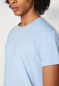 Hellblaue Baumwoll-T-Shirt mit Rundhalsausschnitt, kurzen Ärmeln, glatter Textur und lockerer Passform, die das Seitenprofil des Trägers zeigt.