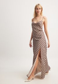 Long brown and cream striped dress with a slight sheen, featuring a ruffled neckline, thin straps, and a thigh-high slit.