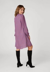 Abito a maniche lunghe di colore viola con un motivo a diamante in rosa e blu, abbinato a stivali neri in suede al ginocchio con tacco a blocco.