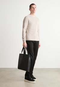 Beige langermet skjorte, svarte bukser, svart lær totebag, og svarte sko med tykke kremfargede såler. Enkelt design, glatt tekstur.