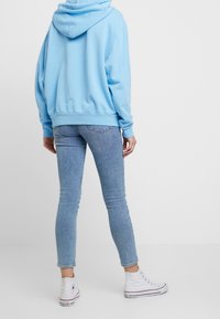 Jasnoniebieska bluza z kapturem o luźnym kroju, zestawiona z jasnoniebieskimi obcisłymi dżinsami. Model nosi białe wysokie trampki.