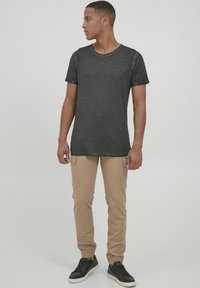 Schwarzes, leichtes T-Shirt mit kurzen Ärmeln und Rundhalsausschnitt, kombiniert mit beigen Jogginghosen mit Taschen und elastischen Bündchen sowie schwarzen Sneakers.