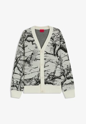 Biała i czarna narzutka z guzikami, z abstrakcyjnym wzorem przypominającym korę drzewa oraz ściągaczami przy mankietach i dolnej krawędzi, oznaczona czerwonym metkiem wewnątrz kołnierza.