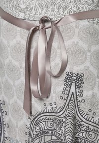 Vestido de algodón con un estampado de cachemira en gris claro y detalles en negro. Cuenta con un cinturón de cinta de satén en rosa claro atado a la cintura.