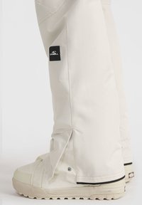 Beige lumilaskuhousut mustalla O'Neill-logolla, joissa on kapeneva muotoilu, napit nilkoissa ja sileä, vettä hylkivä pinta.
