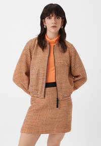 Gequilted bomberjack in een oranje en zwart ruitpatroon, met een ritsluiting, zijzakken en een ontspannen pasvorm, gecombineerd met een bijpassende rok.