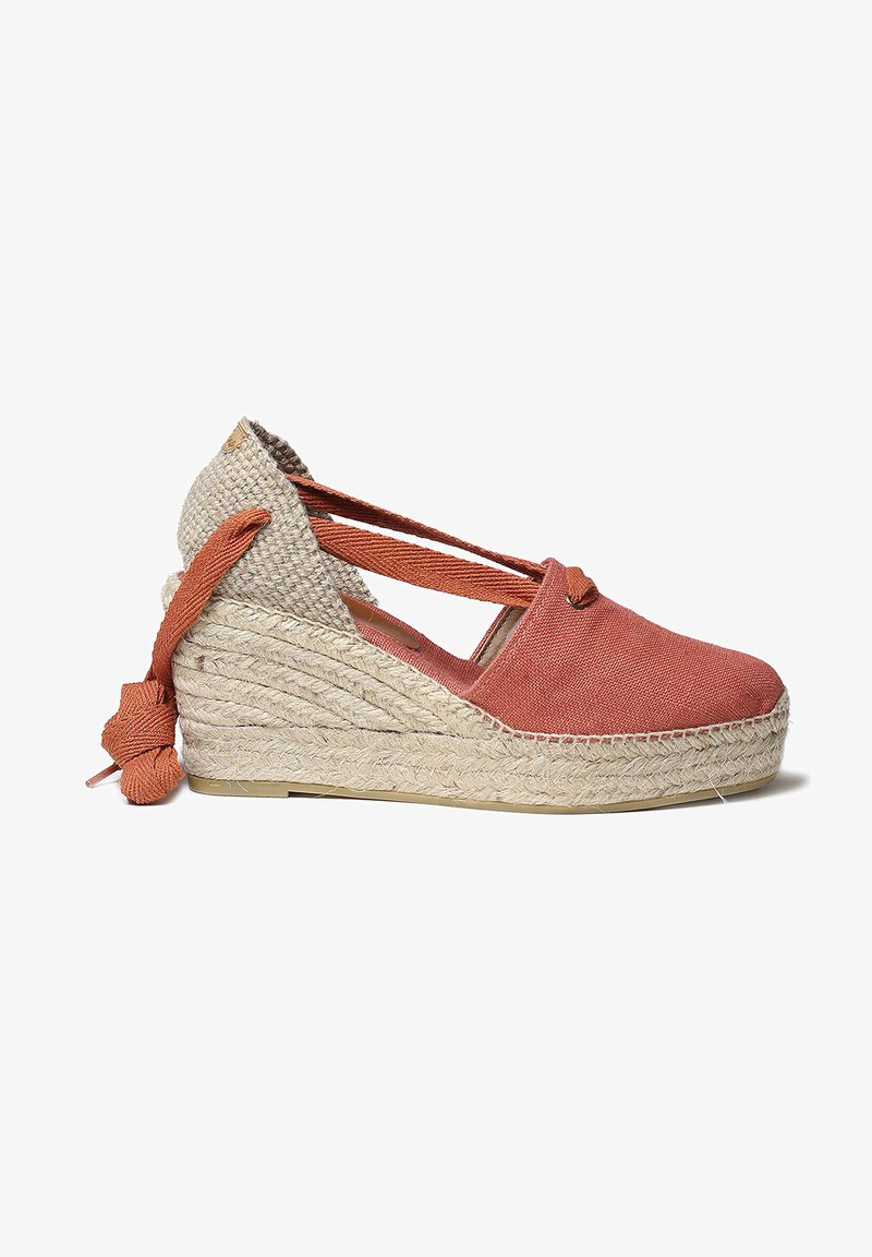 Chaussure à talon compensé en toile corail avec semelle en jute tressé. Elle présente des brides croisées et un nœud décoratif à la cheville pour un maintien sécurisé.