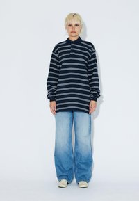 Navy striped long-sleeve polo shirt paired with light blue wide-leg jeans and beige shoes, set against a plain white background.
