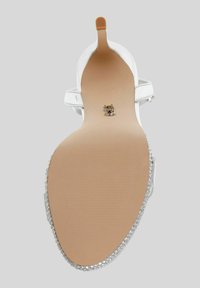 Escarpin blanc à talons hauts avec une tige lisse, une bride de cheville ajustable et un accent en argent texturé sur le talon. Semelle plate beige avec des lignes de grip.