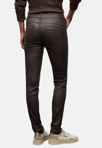 Pantalones marrones ajustados con una textura suave, que cuentan con dos bolsillos traseros y paneles laterales en contraste. Combinados con zapatillas beige.