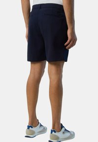 Pantaloni shorts blu navy realizzati in un materiale liscio, con lunghezza a metà coscia, due taschini posteriori e una vestibilità su misura. Abbinati a sneaker bianche e blu.