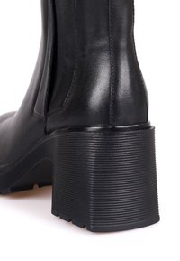 Bottine en cuir noir avec un talon bloc épais à nervures et un détail de panneau latéral élastique.