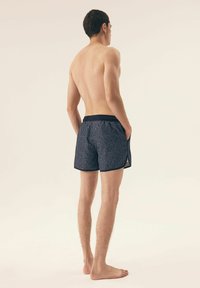 Niebieskie kąpielówki w wzory z teksturowanym wzorem, z jednolitą strefą w pasie i bocznymi kieszeniami, przedstawione z tyłu na neutralnym tle.