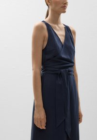 Marineblaue Leinen-Wickeldress mit V-Ausschnitt, breiten Trägern und einem Bindegürtel. Hat eine lockere Passform und eine subtile Textur.