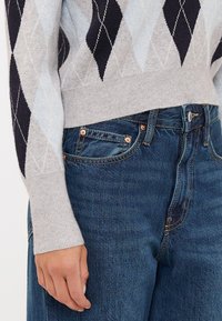 Ανοιχτό γκρι πλεκτό πουλόβερ με ναυτικό μπλε σχέδιο διαμαντιού, σε συνδυασμό με ψηλόμεσα σκούρα μπλε τζην.