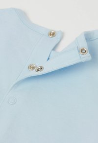 Světle modrá bavlněná košile se zapínáním na tři stříbrné patentky a hladkým povrchem. Kulatý výstřih s mírným překrytím.