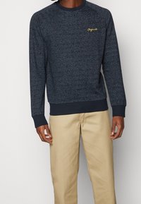 Maglione blu navy con un motivo testurizzato, collo a giro e polsini a coste. Presenta un piccolo ricamo dorato "Originals" sul petto.