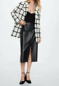 Falda de cuero negra con abertura frontal combinada con un abrigo de tela texturizada en blanco y negro con patrón. Tacones negros completen el atuendo.