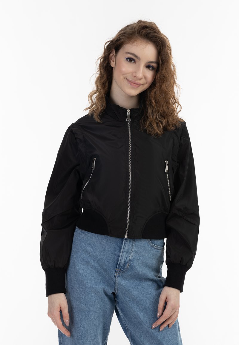 Giacca bomber corta nera con zip frontale e tasche laterali, realizzata in materiale lucido; i polsini e l'orlo a costine migliorano la vestibilità e lo stile.