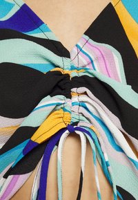 Top multicolor com decote em V e tecido franzido, combinando padrões em preto, teal, amarelo e lavanda, e cordões ajustáveis.