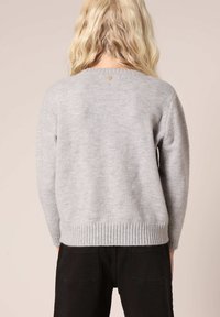 Lichtgrijze trui met een ribbelzoom, lange mouwen en een ronde halslijn. Heeft een kleine knoopdetail op de rug. Gestructureerde stof.