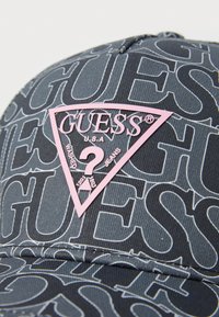 Schwarze Denim-Kappe mit sich wiederholendem "Guess"-Muster, mit einem pinken, dreieckigen Logo-Patch, auf dem "GUESS U.S.A." steht, und Details zu gewaschenen Jeans.