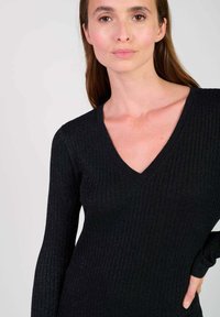 Pull noir côtelé avec un décolleté en V profond et des manches longues, présentant un subtil éclat et une texture douce. Design ajusté qui met en valeur la silhouette.