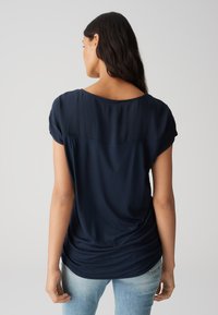 Top blu navy a maniche corte con scollatura arrotondata, dalla texture liscia e dettaglio arricciato sulla parte posteriore, abbinato a jeans azzurri.