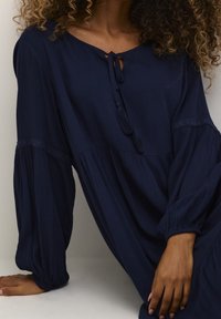 Mörkblå, strukturerad klänning med avslappnad passform, som har en nyckelhålsurringning, knytdetalj och långa ballongärmar.