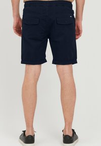 Mørkeblå shorts med en avslappet passform, rullede ermer, to baklommer og elastisk midjebånd, laget av lett bomullsstoff.