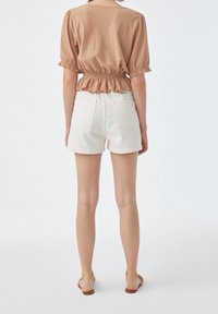 Top corto a maniche corte in tessuto marrone con orlo a peplum, abbinato a pantaloni corti in denim bianchi. Include tasche posteriori e un design casual.