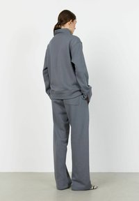 Siva sweatshirta z visokim ovratnikom, sproščenega kroja z rebrastimi manšetami, v kombinaciji z ustreznimi širokimi hlačami. Gladka bombažna mešanica.
