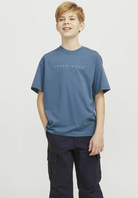 Sinine puuvillane T-särk ümmarguste kaelustega ja lühikeste varrukatega, millel on rinnal valgete tähtedega "JACK & JONES" tekst. Kombineeritud tumehalli cargo pükstega.
