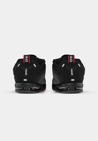 Pantofi sport negri cu un design căptușit, accente roșii distinctive, toc căptușit și o talpă texturată cu elemente de amortizare vizibile.