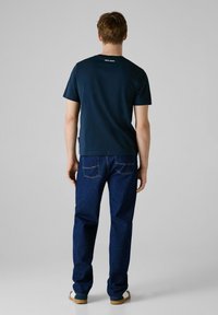 Marineblå kortermet t-skjorte med logo på baksiden, kombinert med mørkeblå denimjeans med baklommer og rette ben.