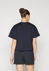 Mörkblå t-shirt med kort ärm och avslappnad passform, rund halsringning och logotypdetalj på vänster ärm. Matchas med svarta shorts.