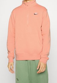 Ljusrosa zip-up sweatshirt med hög krage, ribbade mudd och en ficka framtill. Har en liten svart Nike-logga på bröstet.