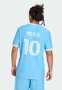 Lyseblå fodboldtrøje med "MESSI" og nummer "10" i hvid, vertikale striber og lyserøde accenter på ærmerne.