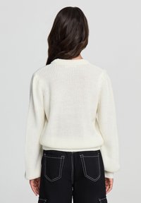 Gruba dzianinowa sweter w kolorze kości słoniowej z okrągłym dekoltem i ściągaczami na rękawach. W połączeniu z czarnymi spodniami, których cechy to widoczne szwy i kieszenie.