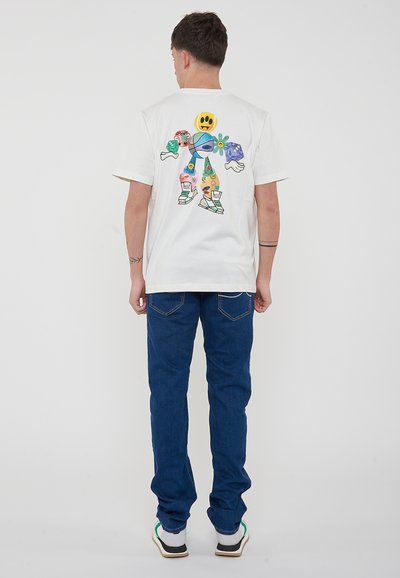 Camiseta de algodón blanca con un diseño colorido y caricaturesco en la parte trasera, combinada con jeans de denim azules y zapatillas blancas.