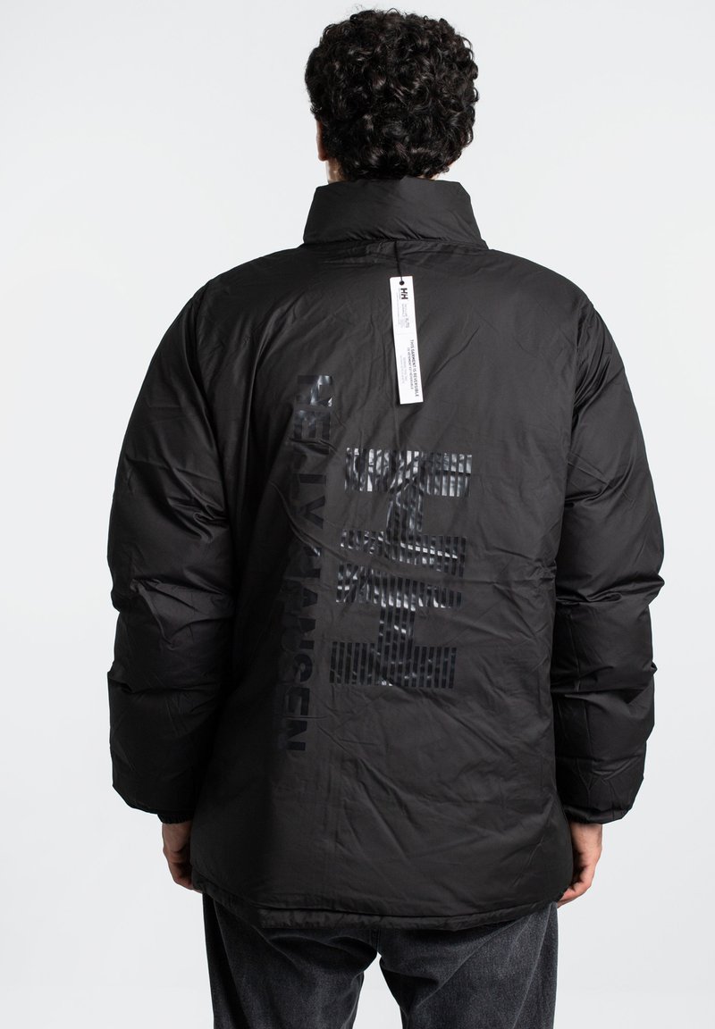 Zwarte pufferjack met hoge kraag en textuur logo op de achterkant, met een matte afwerking en een hangtag. Zacht synthetisch materiaal.