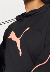 Felpa nera con un prominente logo Puma rosa. Presenta un collo con cordino e una texture liscia. Design minimalista con un vivace contrasto di colori.
