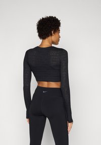 Fekete, hosszú ujjú, crop top, textúrált mintával és látható "NIKE" felirattal; magas derekú fekete leggings-szel párosítva, melyen egy kis logó található.