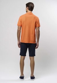 Oranž polo särk kraega, sobitatud tumesiniste lühikestega. Kangas näib pehme ning disain on lihtne ja keha järgnev.