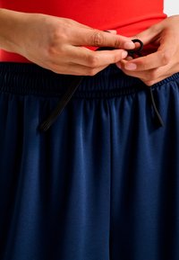 Granatowe spodenki sportowe z elastycznym, marszczonym pasem i czarnym sznurkiem, regulowane przez ręce. Gładki, lekki materiał.